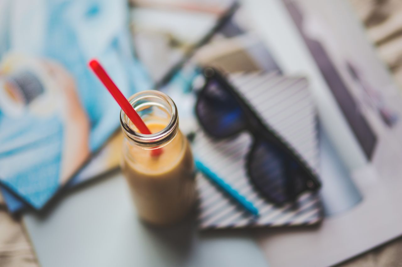 A refreshing smoothie with red straw on an artistic desk setup featuring sunglasses and stationery.