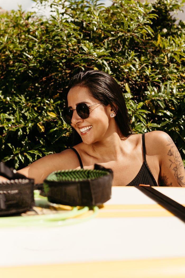 contact-img Cheerful woman with a tattoo smiling in sunglasses, enjoying a sunny day outdoors.