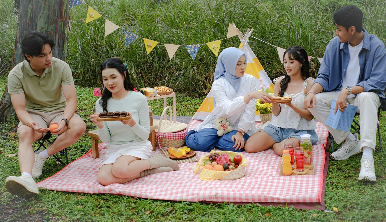 ours-journey Five friends having a picnic on a sunny day with food and decorations.